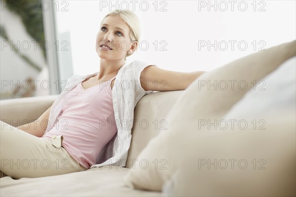 Blond woman daydreaming on couch. Photo : momentimages