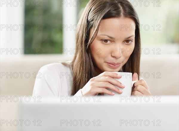 Woman drinking coffee while browsing the internet. Photo. momentimages