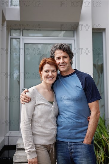 Happy couple standing with their arms around one another. Photo : momentimages