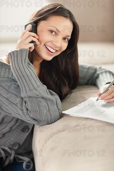 Woman talking on phone while doing paperwork. Photo : momentimages