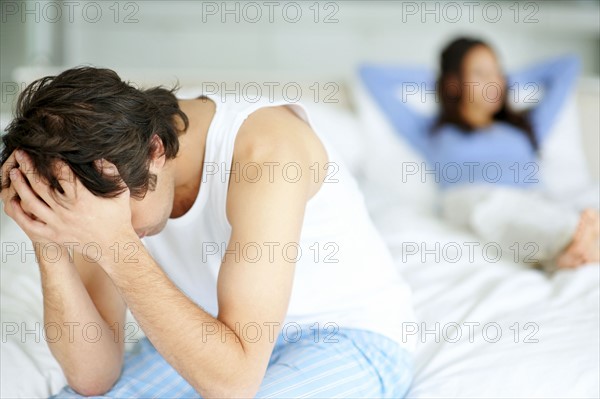 Frustrated man sitting on edge of bed. Photo. momentimages