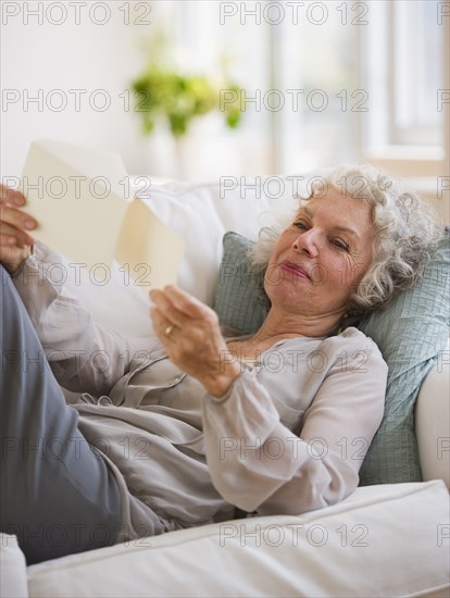 Woman reading mail while relaxing on couch. Photo. Daniel Grill