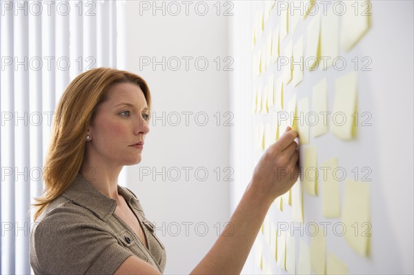 Businesswoman putting sticky note on wall.