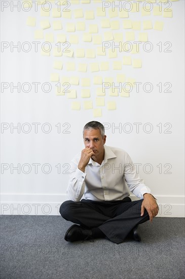 Businessman sitting behind wall covered in sticky notes.