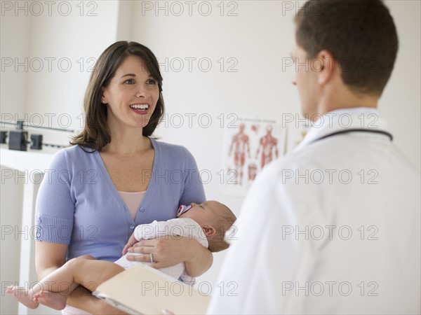 Woman holding baby while talking to doctor.