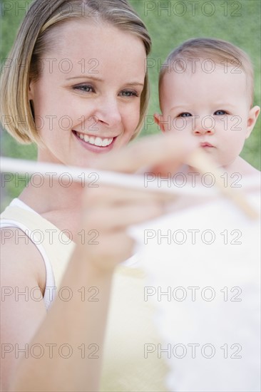 Mother holding baby while hanging up the laundry. Photo. Jamie Grill