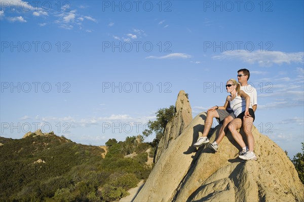 Couple relaxing on peak of rock.