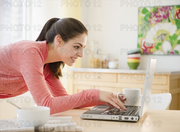Woman typing on laptop in kitchen. Photo : Jamie Grill