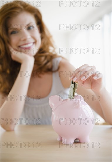 Woman putting money in piggy bank. Photo. Jamie Grill
