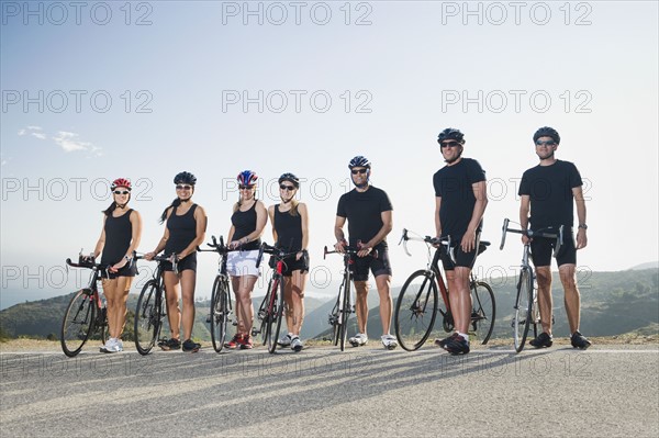 Cyclists standing beside their bikes on the side of the road.