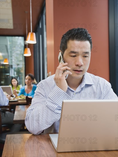 Man talking on phone and working on laptop in restaurant.