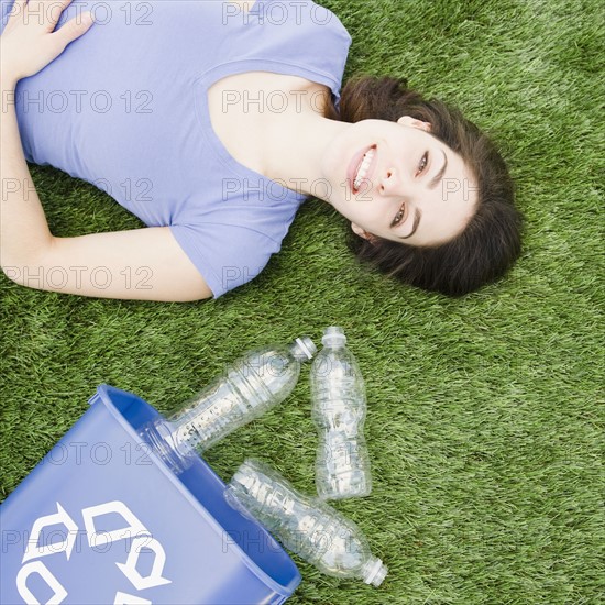 Woman lying on grass beside recycling bin. Photo. Jamie Grill