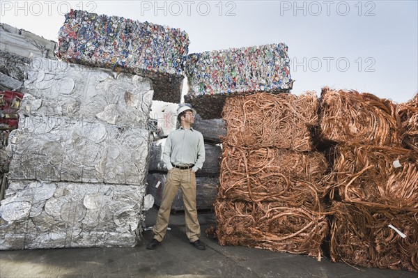 Worker standing beside stacks of recycled material.
