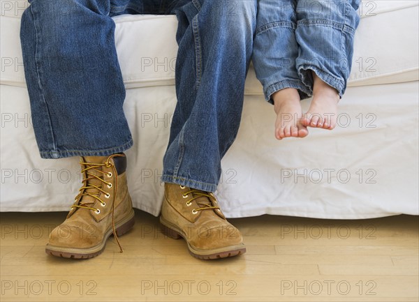 Legs of two people sitting on couch.