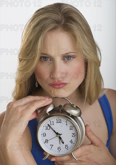 Upset blond woman holding an alarm clock.