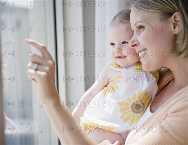 Mother and baby daughter looking out window. Photo : Jamie Grill