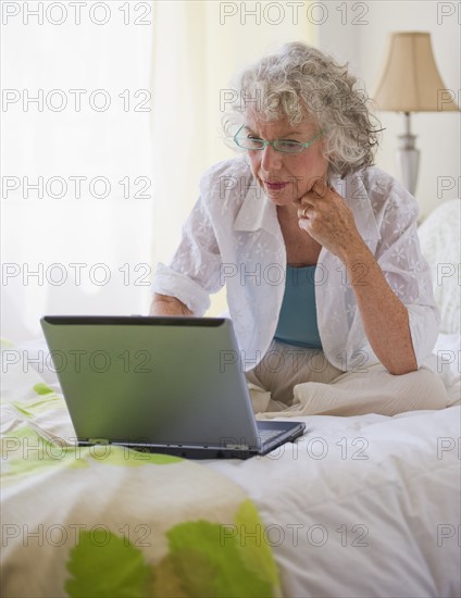 Woman looking at laptop in bedroom. Photo : Daniel Grill