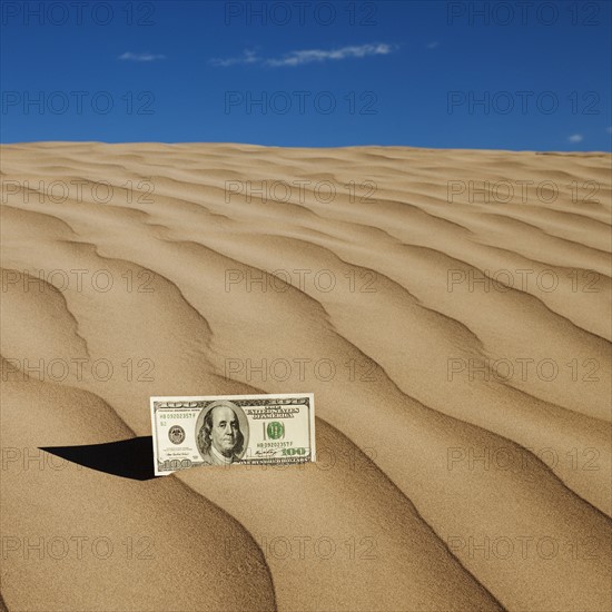 100 dollar bill on sand in desert. Photo : Mike Kemp