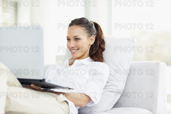 Woman relaxing on couch with laptop. Photo. momentimages