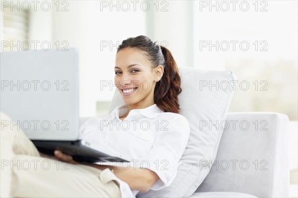 Woman relaxing on couch with laptop. Photo : momentimages