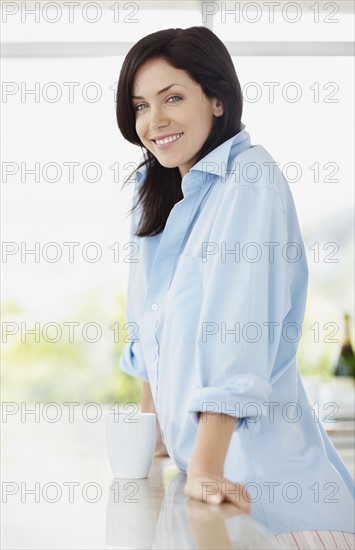 Brunette woman leaning on kitchen counter. Photo : momentimages