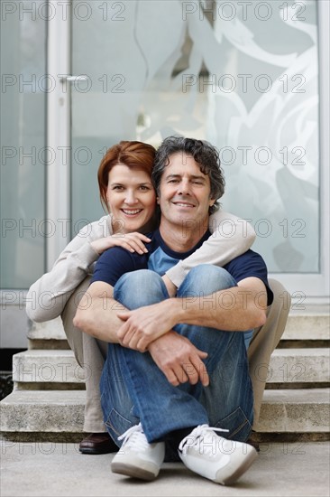 Couple sitting on steps in front of their home. Photo : momentimages