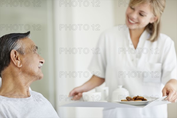 Nurse giving tray of food to patient. Photo. momentimages