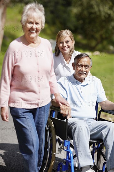 Two women walking with man in a wheelchair. Photo. momentimages