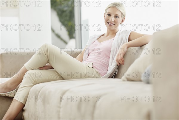 Pretty blond woman sitting on couch. Photo : momentimages