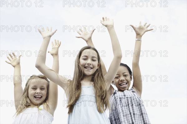Three young girls with their arms raised. Photo. momentimages