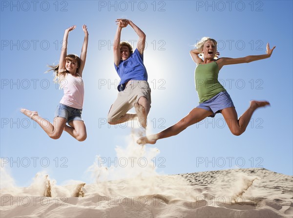 Three people jumping in the sand. Photo : Mike Kemp