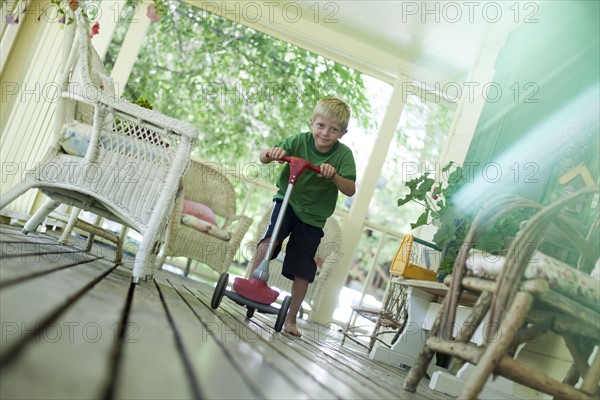 Little boy riding scooter on porch. Photo : Tim Pannell
