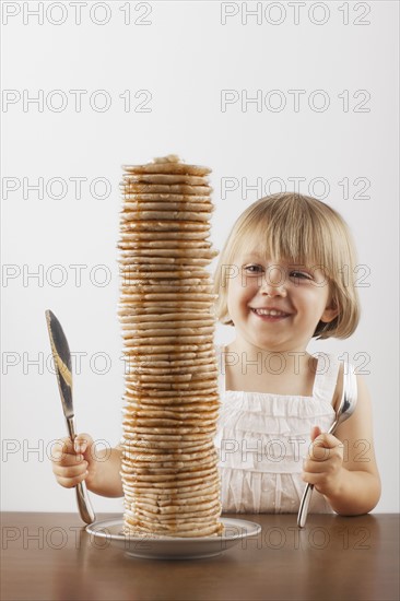 Young girl sitting behind a tall stack of pancakes. Photo : FBP