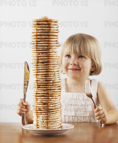 Young girl sitting behind a tall stack of pancakes. Photo : FBP