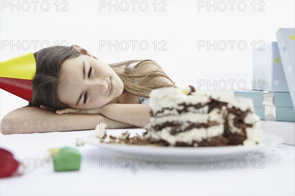 Tired young girl looking at birthday cake. Photo : momentimages