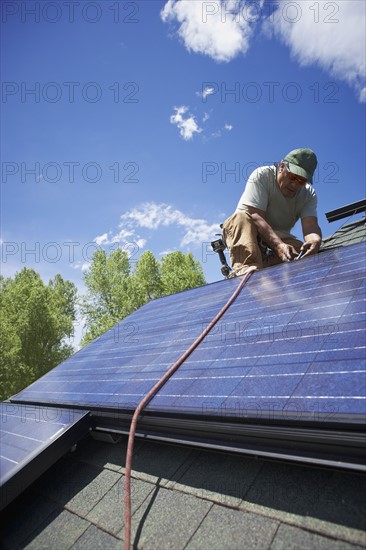 Construction worker installing solar panel on roof. Photo. Shawn O'Connor