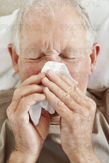 Senior man blowing his nose. Photo. momentimages