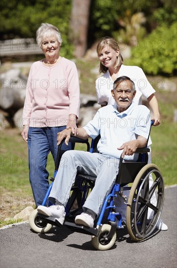 Two women walking with man in a wheelchair. Photo. momentimages