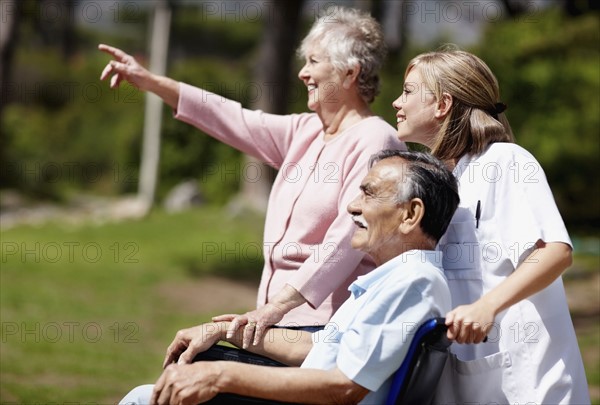 Two woman out for a walk with man in a wheelchair. Photo. momentimages