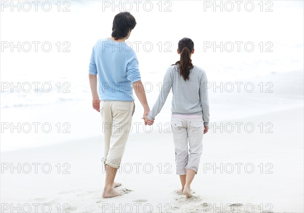 Couple walking barefoot on the beach. Photo. momentimages