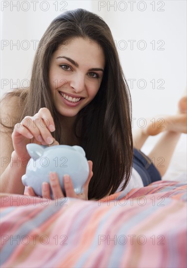 Woman putting coins in piggy bank. Photo : Jamie Grill