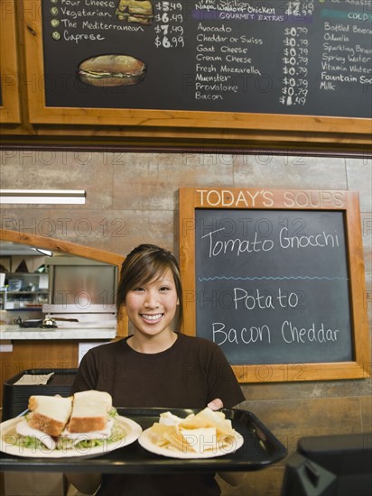 Woman holding tray of food in bakery.