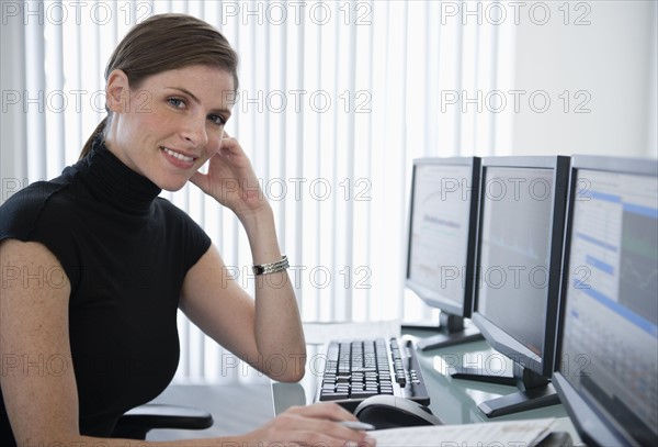 Woman in office sitting at desk with computers.