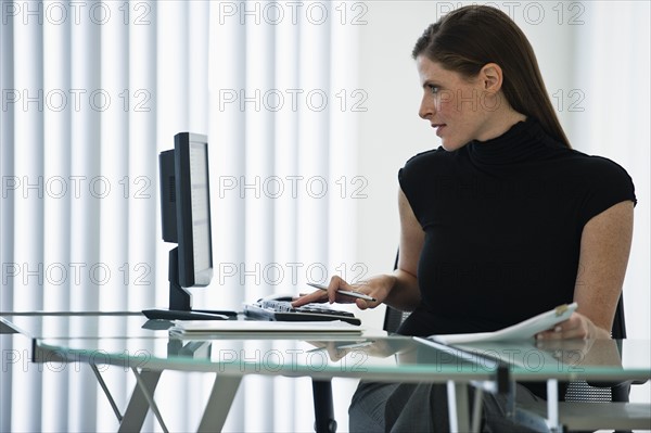 Woman in office working at desk with laptop.