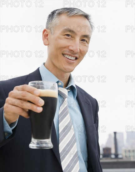 Businessman holding pint of ale and looking at camera. Photo : Jamie Grill