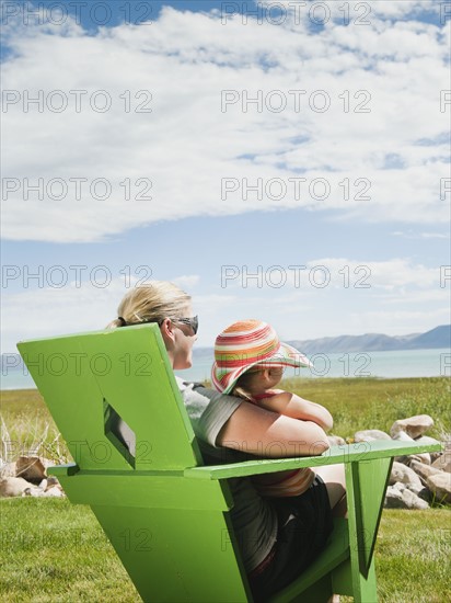 Mother and daughter (2-3) sitting on chair and looking at view.