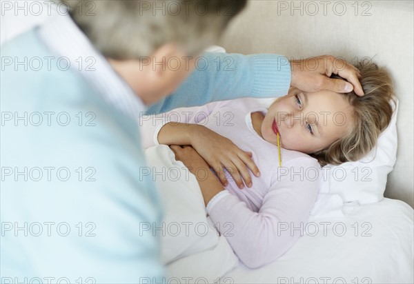 Grandfather tending granddaughter (10-11) lying in bed with thermometer in mouth. Photo : Momentimages