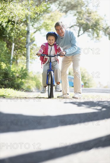 Grandfather helping granddaughter (10-11) riding bike. Photo : Momentimages