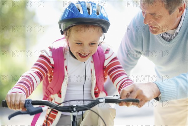 Grandfather helping granddaughter (10-11) riding bike. Photo : Momentimages