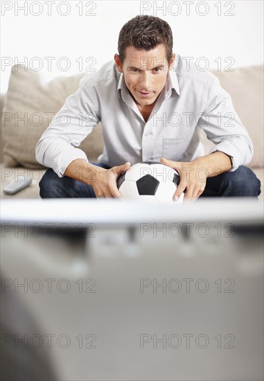 Mid adult man watching football match on television. Photo : Momentimages